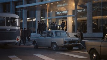 Movie still from “Playtime” (1967), directed by Jacques Tati – A car parked on the side of the street in front of a building; Extreme Wide shot, Low angle