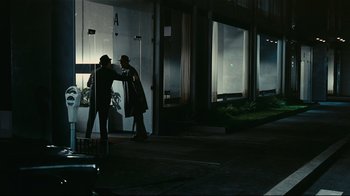 Movie still from “Playtime” (1967), directed by Jacques Tati – Two men are walking down the street at night; Wide shot, Over the shoulder angle