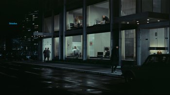 Movie still from “Playtime” (1967), directed by Jacques Tati – A group of people standing on the sidewalk in front of a building at night; Extreme Wide shot, High angle