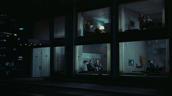 Movie still from “Playtime” (1967), directed by Jacques Tati – A group of people sitting in a room at night; Extreme Wide shot, High angle