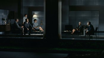 Movie still from “Playtime” (1967), directed by Jacques Tati – A group of people sitting on a couch in the dark; Wide shot, High angle