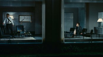 Movie still from “Playtime” (1967), directed by Jacques Tati – A woman sitting on a chair in front of a window; Wide shot, High angle