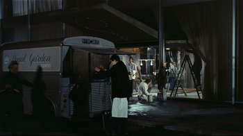 Movie still from “Playtime” (1967), directed by Jacques Tati – A group of people preparing food on a grill; Wide shot, High angle