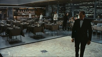Movie still from “Playtime” (1967), directed by Jacques Tati – A group of people standing in a room with tables; Wide shot, High angle