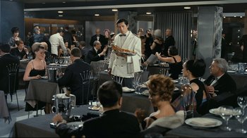 Movie still from “Playtime” (1967), directed by Jacques Tati – A group of people sitting at tables in a room; Wide shot, High angle