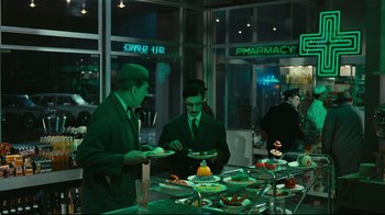 Movie still from “Playtime” (1967), directed by Jacques Tati – Two men in suits and hats are serving food to people; Wide shot, High angle