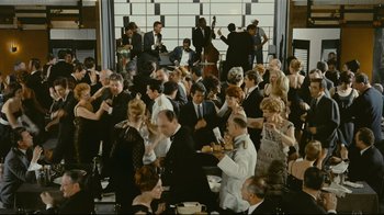 Movie still from “Playtime” (1967), directed by Jacques Tati – A large group of people gathered in a room; Extreme Wide shot, High angle