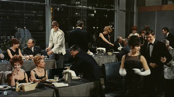 Movie still from “Playtime” (1967), directed by Jacques Tati – A group of people sitting at tables with plates of food in front of them; Wide shot, High angle