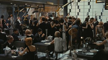 Movie still from “Playtime” (1967), directed by Jacques Tati – A large group of people sitting at tables in a room; Wide shot, High angle