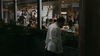 Movie still from “Playtime” (1967), directed by Jacques Tati – A man in a white jacket is standing in front of a mirror; Wide shot, Over the shoulder angle
