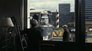 Movie still from “Playtime” (1967), directed by Jacques Tati – A man standing in front of a bus on the side of the road; Wide shot, Over the shoulder angle