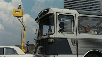 Movie still from “Playtime” (1967), directed by Jacques Tati – A man standing next to a bus on a city street; Extreme Wide shot, Low angle