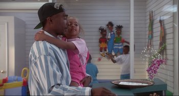 Movie still from “Poetic Justice” (1993), directed by John Singleton – A man holding a little girl in his arms at a table; Medium shot, Over the shoulder angle