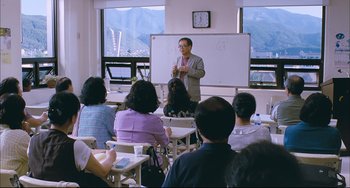 Movie still from “Poetry” (2010), directed by Lee Chang-dong – A man standing in front of a group of people in a room; Wide shot, High angle