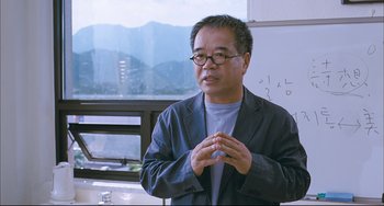 Movie still from “Poetry” (2010), directed by Lee Chang-dong – An asian man wearing glasses and a gray jacket; Medium shot, Low angle