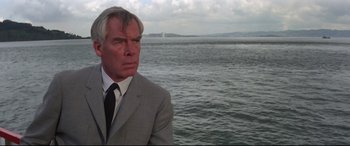 Movie still from “Point Blank” (1967), directed by John Boorman – A man wearing a suit and tie standing in front of a body of water; Close Up shot, Low angle