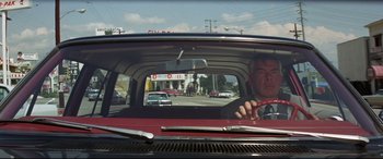 Movie still from “Point Blank” (1967), directed by John Boorman – A man driving in a red car on the street; Medium shot, Low angle