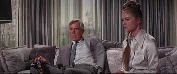 Movie still from “Point Blank” (1967), directed by John Boorman – A man in a gray suit sitting on a couch next to a woman in a white dress; Medium shot, Over the shoulder angle