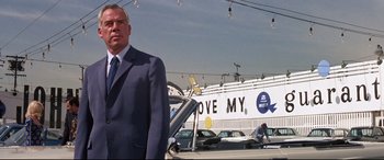 Movie still from “Point Blank” (1967), directed by John Boorman – A man in a suit and tie standing in front of cars; Medium shot, Low angle