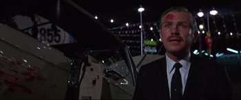 Movie still from “Point Blank” (1967), directed by John Boorman – A man in a black suit and a red spot on his forehead; Close Up shot, Low angle