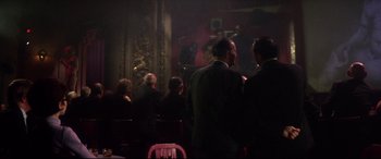 Movie still from “Point Blank” (1967), directed by John Boorman – A group of people sitting in front of microphones in a room; Wide shot, Over the shoulder angle