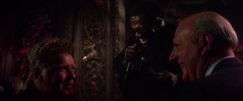 Movie still from “Point Blank” (1967), directed by John Boorman – A man in a black shirt is singing into a microphone; Close Up shot, Over the shoulder angle