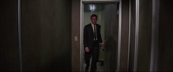 Movie still from “Point Blank” (1967), directed by John Boorman – A man in a suit and tie standing in front of a door; Wide shot, High angle