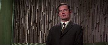Movie still from “Point Blank” (1967), directed by John Boorman – A man wearing a suit and tie standing in front of a wall; Close Up shot, Low angle