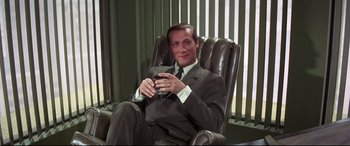 Movie still from “Point Blank” (1967), directed by John Boorman – A man in a suit and tie holding a glass of wine; Medium shot, High angle
