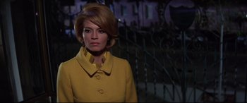 Movie still from “Point Blank” (1967), directed by John Boorman – A woman in a yellow coat standing in front of a fence; Medium shot, Low angle