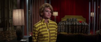 Movie still from “Point Blank” (1967), directed by John Boorman – A woman in a yellow and brown striped shirt standing next to a bed; Medium shot, Low angle
