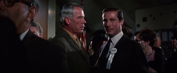 Movie still from “Point Blank” (1967), directed by John Boorman – Two men standing next to each other in front of an american flag; Close Up shot, Over the shoulder angle