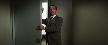 Movie still from “Point Blank” (1967), directed by John Boorman – A man in a suit and tie standing in front of an open door; Medium shot, Low angle