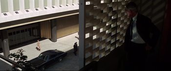 Movie still from “Point Blank” (1967), directed by John Boorman – A man standing next to a car in front of a building; Extreme Wide shot, High angle