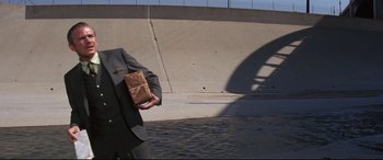 Movie still from “Point Blank” (1967), directed by John Boorman – A man in a suit holding a bag in his hand; Medium shot, Low angle