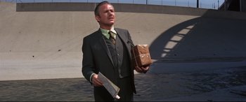 Movie still from “Point Blank” (1967), directed by John Boorman – A man in a suit and tie holding papers and a brown bag; Medium shot, Low angle