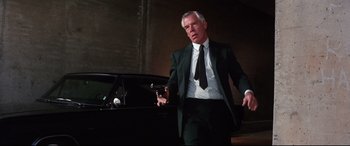 Movie still from “Point Blank” (1967), directed by John Boorman – A man in a suit and tie standing in front of a car; Medium shot, Low angle