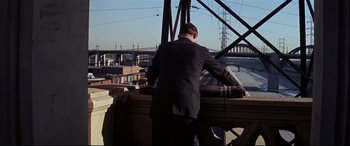 Movie still from “Point Blank” (1967), directed by John Boorman – A man in a suit standing on top of a bridge; Wide shot, Low angle