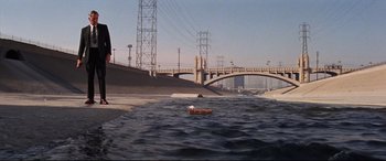Movie still from “Point Blank” (1967), directed by John Boorman – A boat floating on top of a body of water near a bridge; Extreme Wide shot, High angle