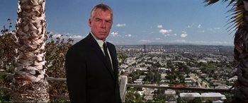 Movie still from “Point Blank” (1967), directed by John Boorman – A man in a suit and tie standing in front of a city; Medium shot, Low angle