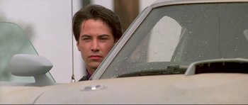Movie still from “Point Break” (1991), directed by Kathryn Bigelow – A man in a suit leaning up against a car window; Close Up shot, Low angle