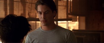 Movie still from “Point Break” (1991), directed by Kathryn Bigelow – A young man in a gray shirt is looking to his left; Close Up shot, Over the shoulder angle