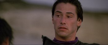 Movie still from “Point Break” (1991), directed by Kathryn Bigelow – A man with long black hair wearing a purple shirt; Close Up shot, Low angle