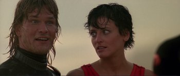 Movie still from “Point Break” (1991), directed by Kathryn Bigelow – A woman in a red top looking at the camera; Close Up shot, Over the shoulder angle