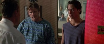 Movie still from “Point Break” (1991), directed by Kathryn Bigelow – Two men standing next to each other in front of a wall; Medium shot, Over the shoulder angle