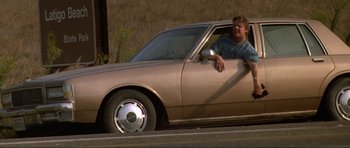 Movie still from “Point Break” (1991), directed by Kathryn Bigelow – A man sitting in the driver's seat of a parked car; Wide shot, Low angle