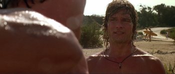 Movie still from “Point Break” (1991), directed by Kathryn Bigelow – A man with long blonde hair and a necklace on; Close Up shot, Over the shoulder angle