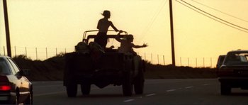Movie still from “Point Break” (1991), directed by Kathryn Bigelow – Two people riding in the back of a truck on a highway; Wide shot, Low angle