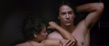 Movie still from “Point Break” (1991), directed by Kathryn Bigelow – A man and a woman embracing in a dark room; Close Up shot, Overhead angle