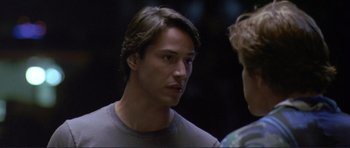 Movie still from “Point Break” (1991), directed by Kathryn Bigelow – A man with a braid is talking to another man; Close Up shot, Over the shoulder angle